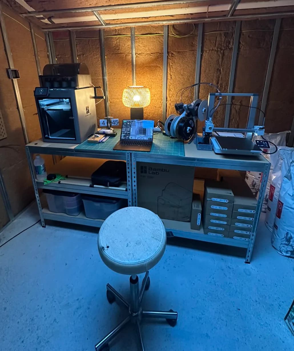 L'établi de l'atelier : deux imprimantes 3D à filament, l'ordinateur, une lampe et les bobines rangées dessous