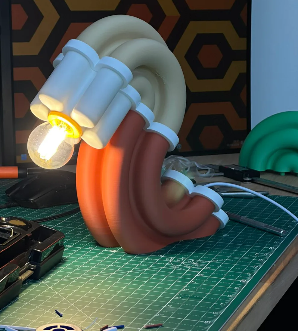 Lampe à poser faite de gros tubes arrondis beige, blancs et terracotta, ampoule allumée, sur l'établi