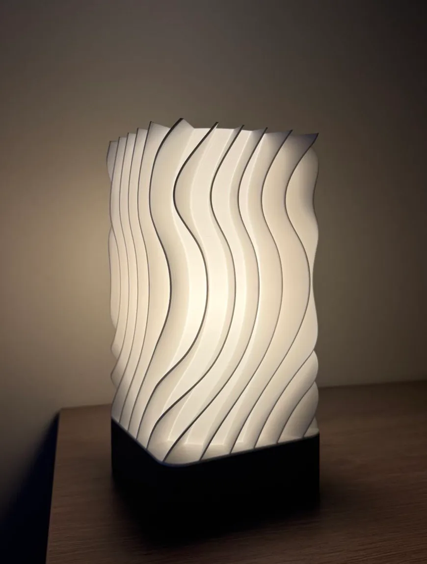 Lampe de chevet allumée, faite de lamelles ondulées blanches sur un socle noir